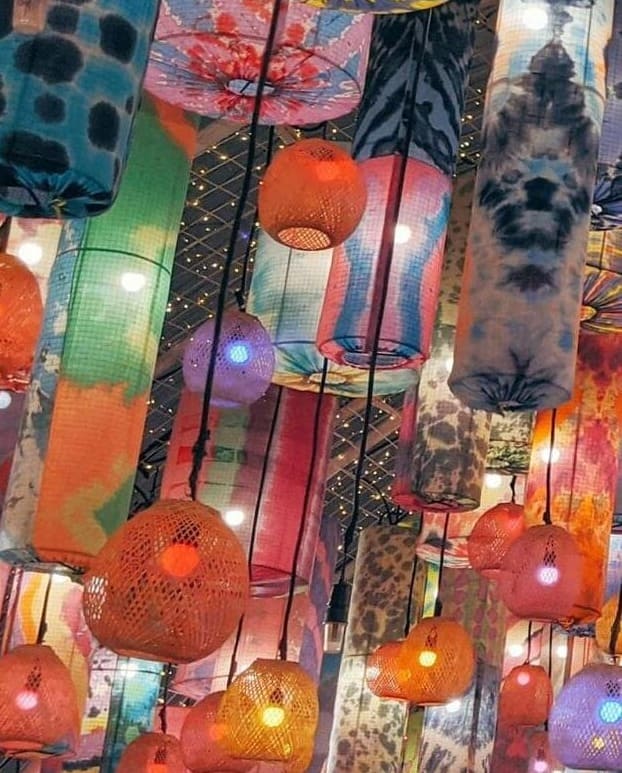 Lampade cilindriche e intrecciate appese al soffitto, illuminate da luci calde e decorate con motivi colorati.